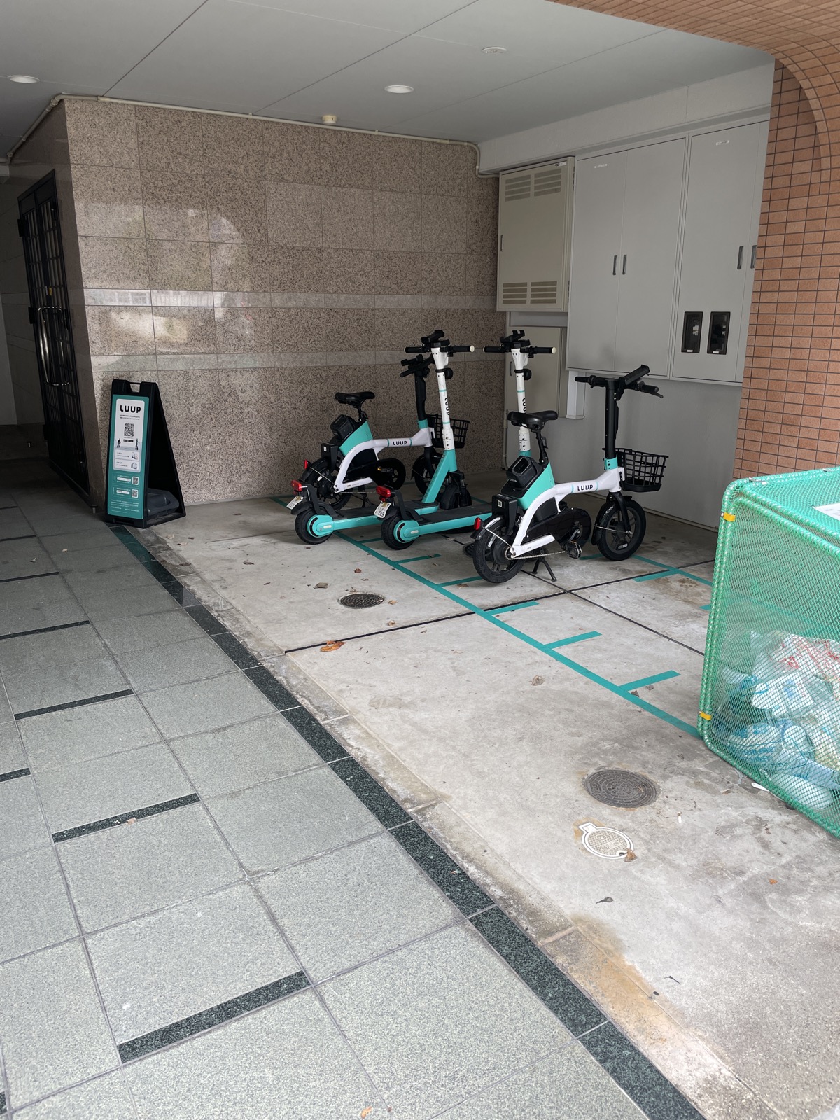 ビルの入口脇に枠線を引いて並べられた電動キックボードと電動自転車